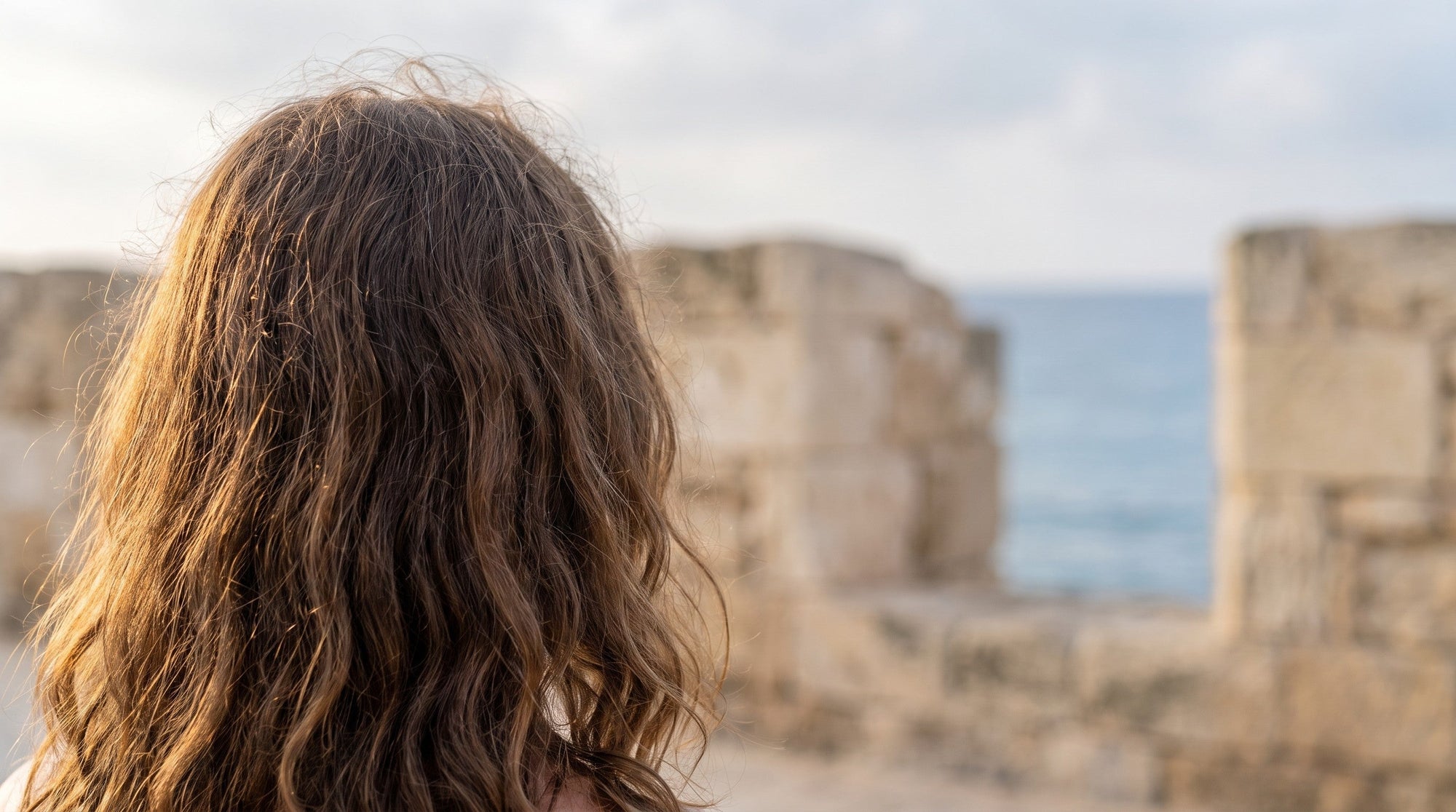 Wavy hair seen from behind on a Cyprus seafront in humid coastal light, anti-frizz hair care in Cyprus