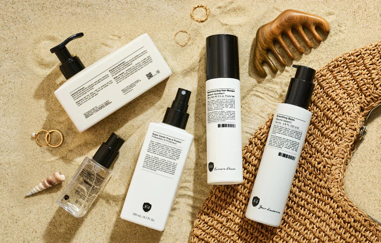 Number 4 hair care products styled on Mediterranean beach sand with a wooden comb, shells and a straw bag, available at WOOP Cyprus